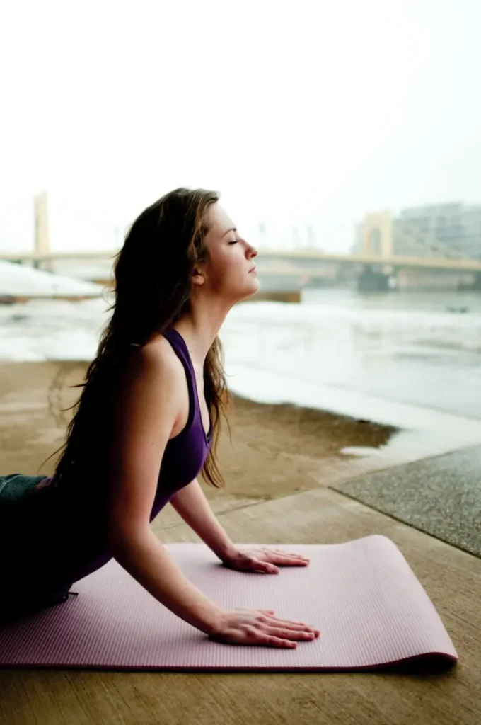 A women in a purple tank top on a lavender yoga mat practicing the cobra yoga pose