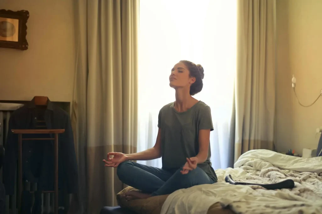 A woman sitting on her bed with her palms on her knees facing up doing transcendental meditation