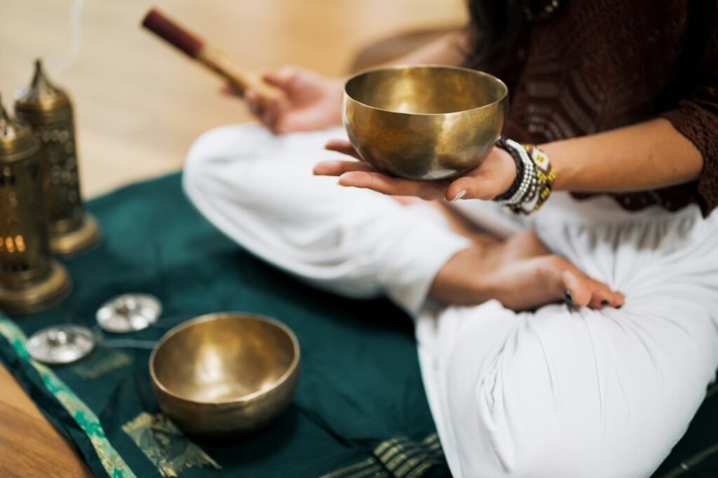 person in white pants holding a tibetan singing bowl and practicing deep impact meditation
