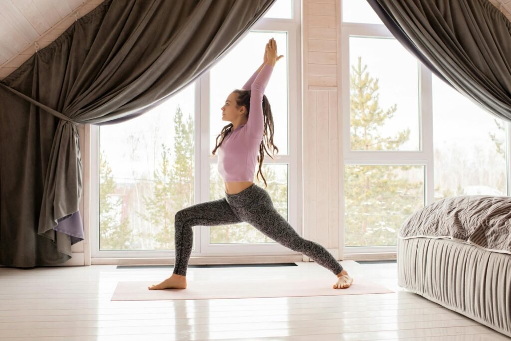 A woman near windows in a warrior one yoga pose