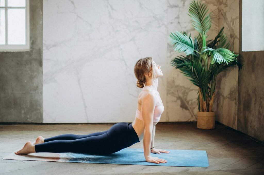 A woman in a pink sports bra and black leggings doing yoga cobra pose on a yoga mat