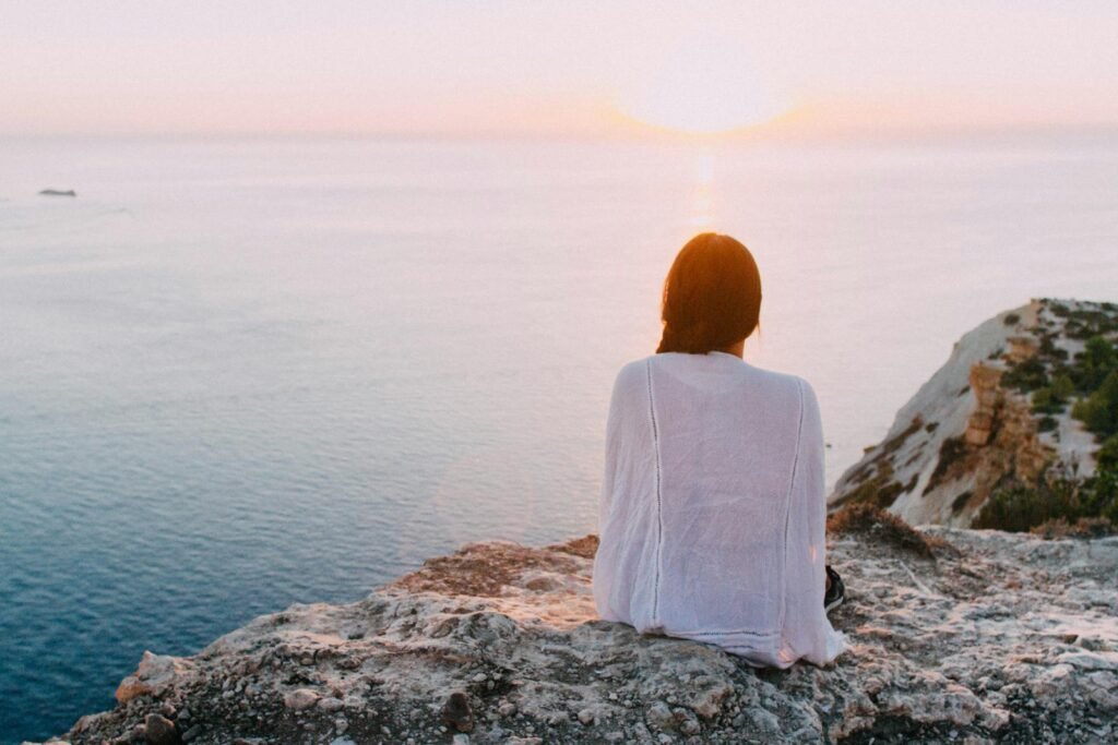 A woman sitting on gray rocks near a body of water