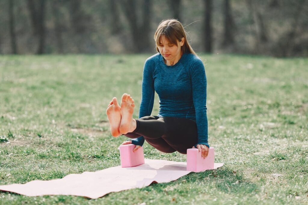 Full body barefoot sportswoman in sportswear doing yoga arm exercise on sport mat during training on lawn in park adhering to healthy lifestyle while looking down