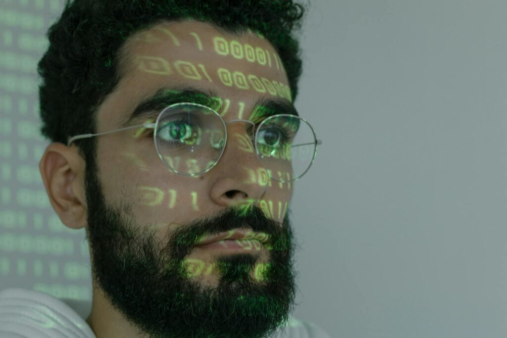 A bearded man wearing glasses with focused attention on a computer monitor