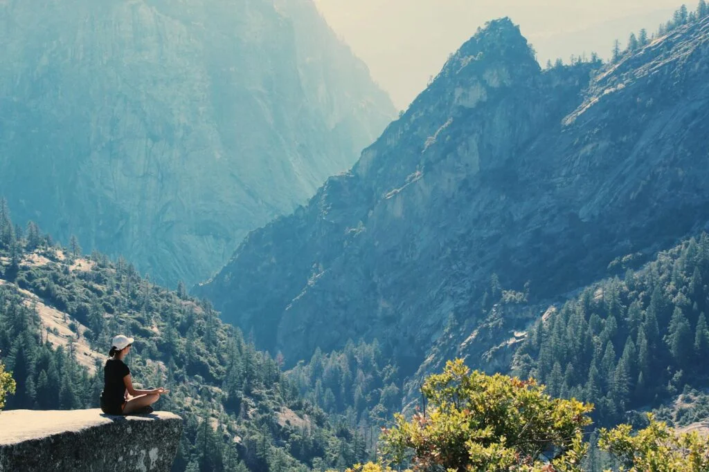 A woman practicing the stunning spectrum of meditation in front of a mountain view