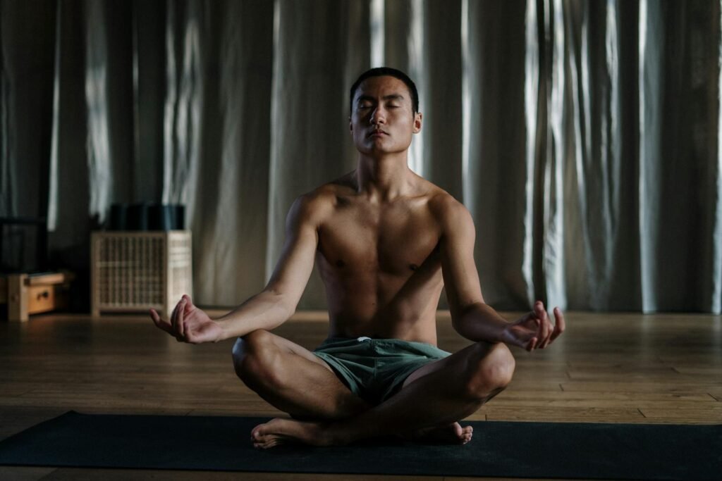 A topless man sitting on the floor meditating in one of many popular yoga poses