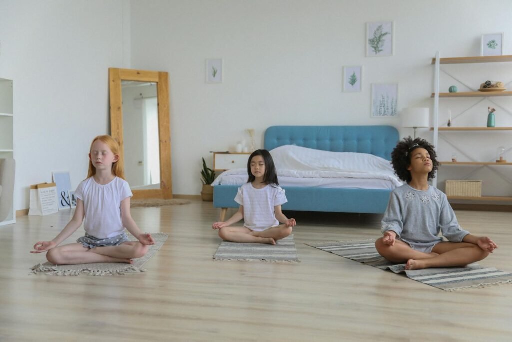 Three children meditating in a bright room with eyes closed and arms folded on crossed legs