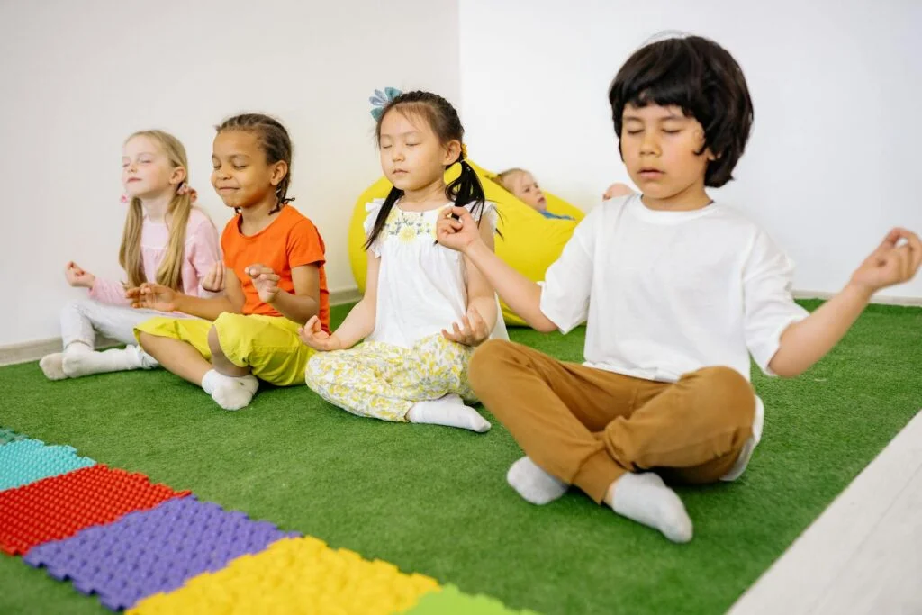 Four children In legs criss-cross position with closed eyes practicing meditation for kids