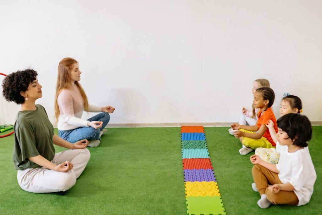 Two teachers and four children are sitting on the floor learning yoga poses for kids