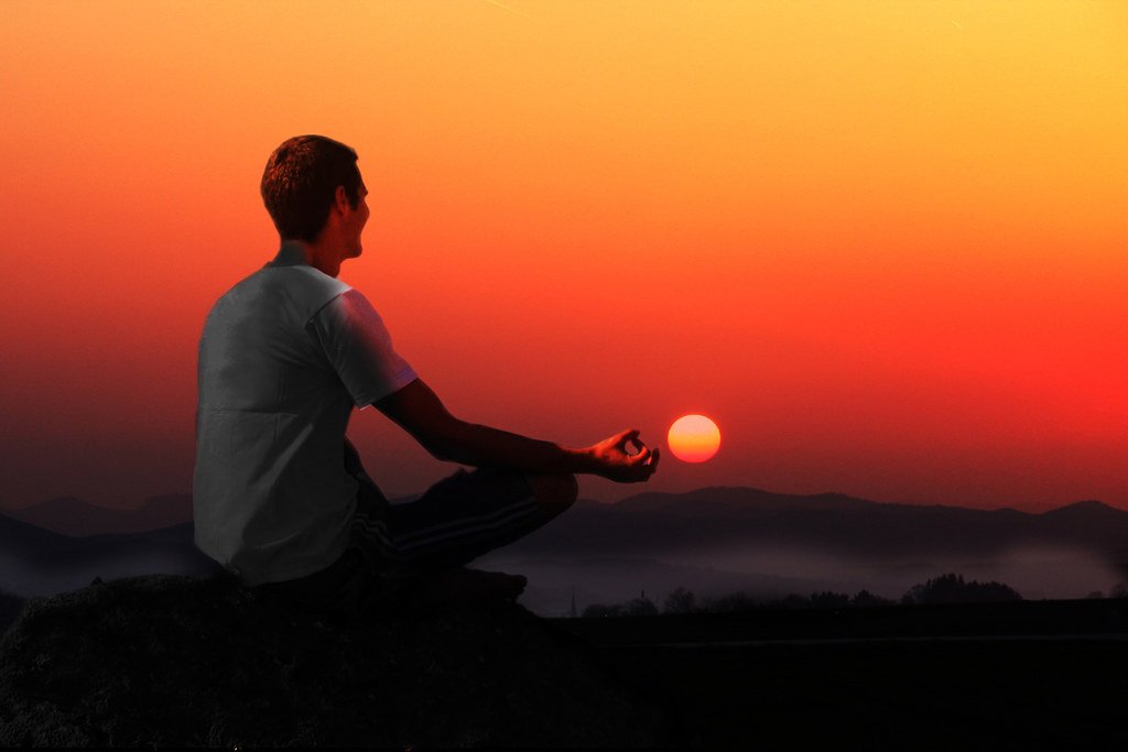 A man meditating during a sunset from one of several popular yoga poses