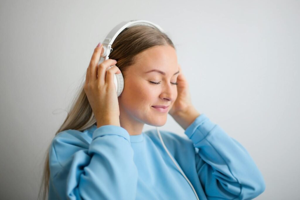 A woman in a blue sweatshirt listening to meditation music with white headphones