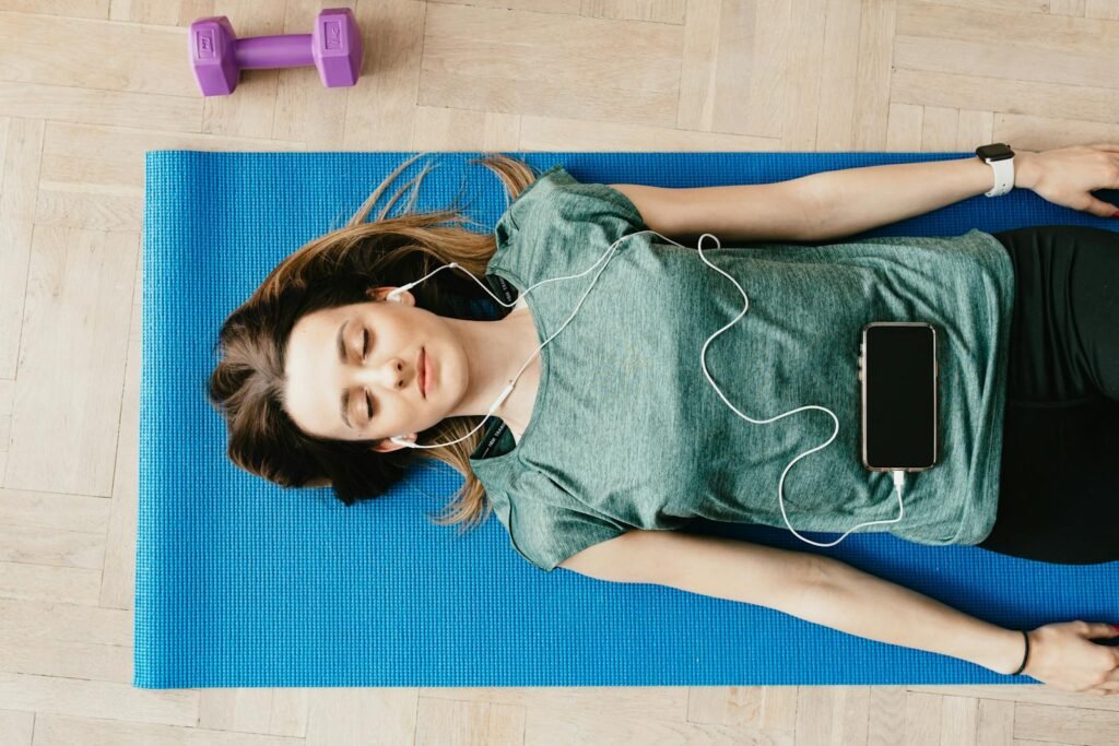 A peaceful woman listening to guided meditation with earphones resting in Shavasana pose at home